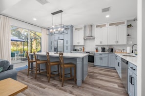 A modern kitchen with grey cabinets, a central island, and a dining area with wooden chairs.