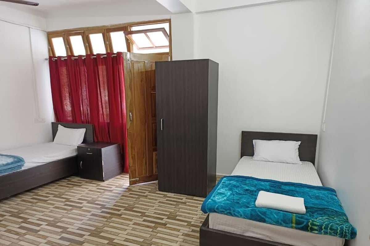 A room with two beds, a wardrobe, and a window with curtains.