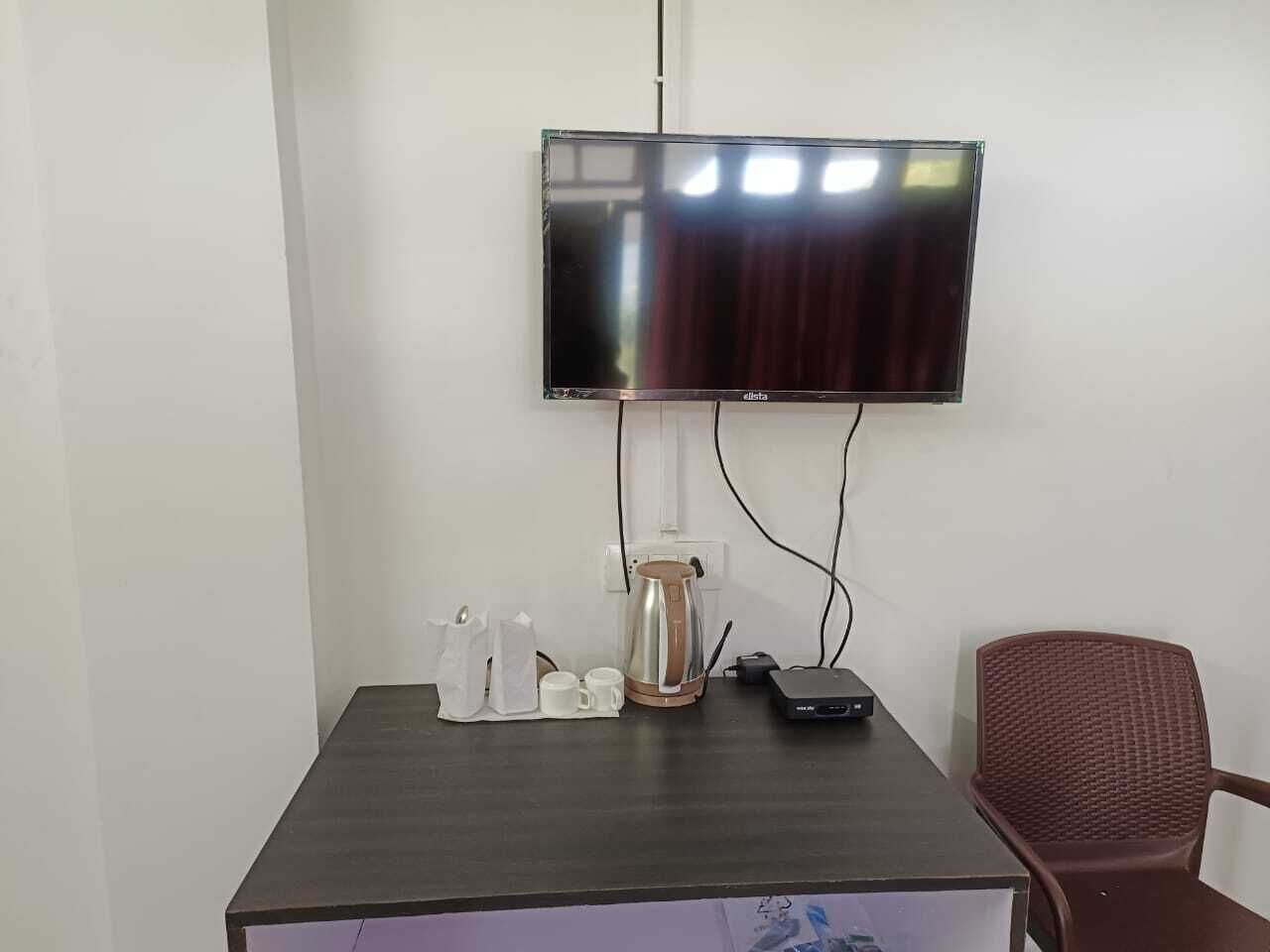 Une chambre dotée d’un téléviseur à écran plat fixé au mur, d’une machine à café, d’une multiprise et d’un fauteuil rouge.