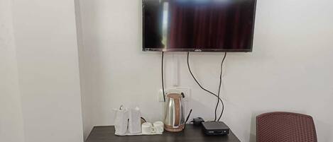 A room with a flat-screen TV mounted on the wall, a coffee maker, a power strip, and a red chair.