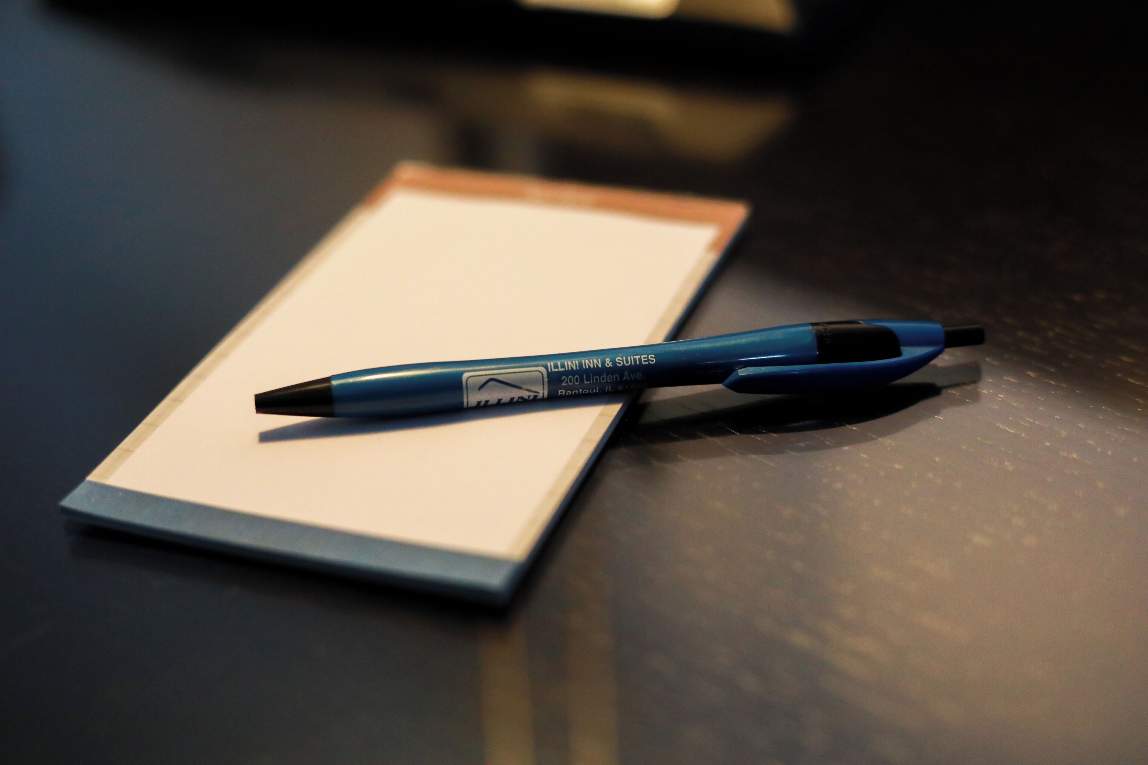 Un bolígrafo azul con una etiqueta sobre una superficie oscura, posiblemente una mesa o escritorio.