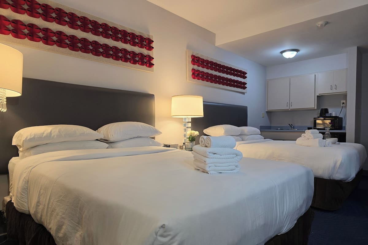 A hotel room with two beds, a flat-screen TV, a microwave, and a small kitchenette.