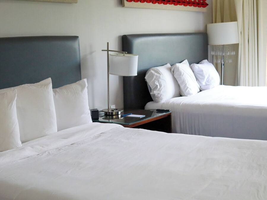 Habitación de hotel con dos camas, una mesita de noche con lámpara y un reloj de pared.