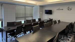 Une salle de conférence avec une longue table, des chaises, un téléviseur et une pancarte « bienvenue » accrochée au mur.