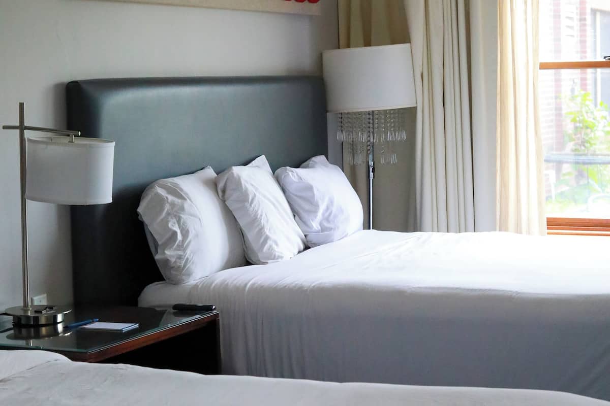 A hotel room with two beds, a large abstract art piece on the wall, and a view of the outdoors through the window.