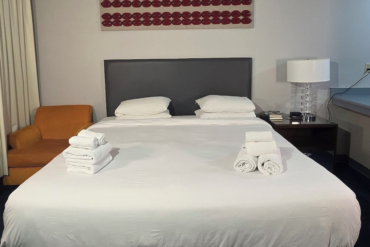 A hotel room with a large bed, a headboard, a nightstand, a lamp, and a chair.