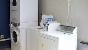 Un espace buanderie comprenant des machines à laver superposées et un sèche-linge, un panneau de commande et une prise électrique au mur.