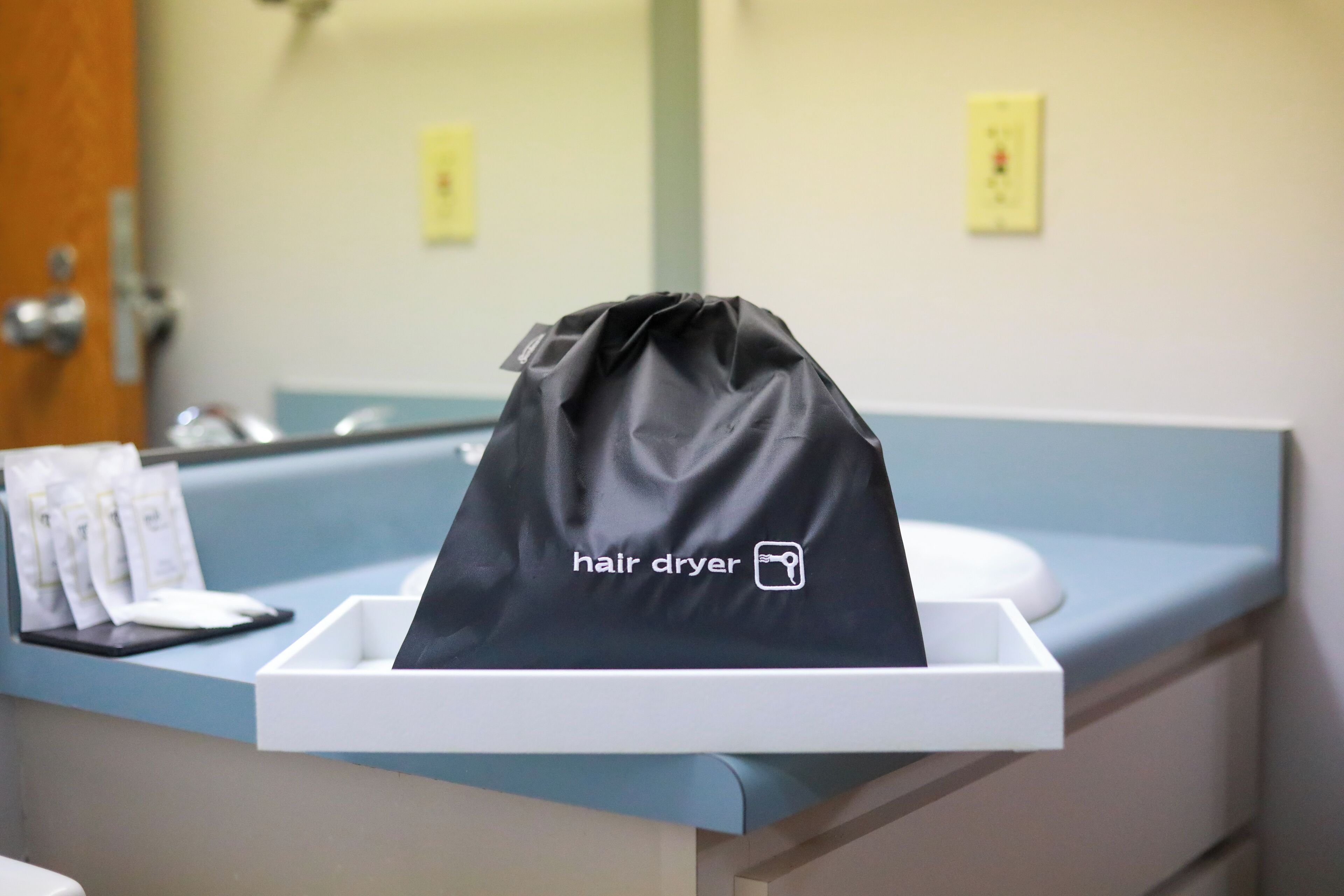 A hair dryer bag on a counter with a sink and mirror in the background.