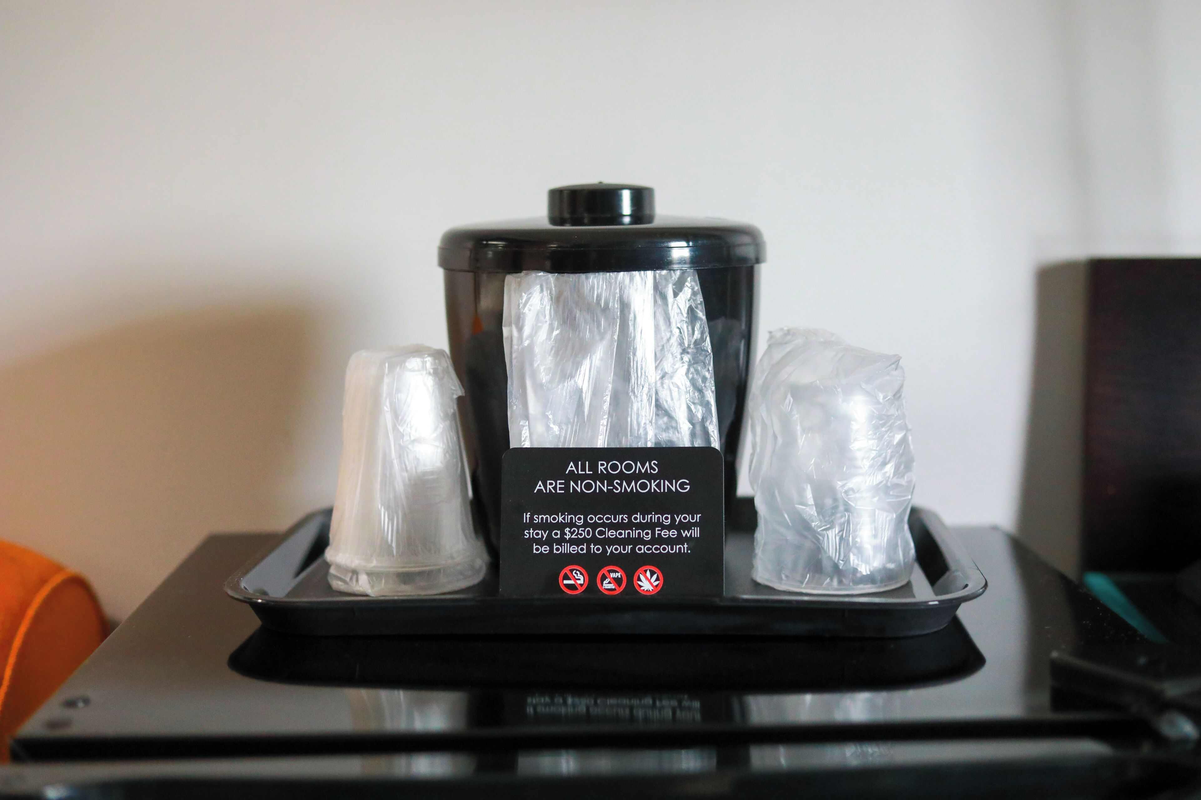A non-smoking sign on a tray with a black container and two clear plastic cups.