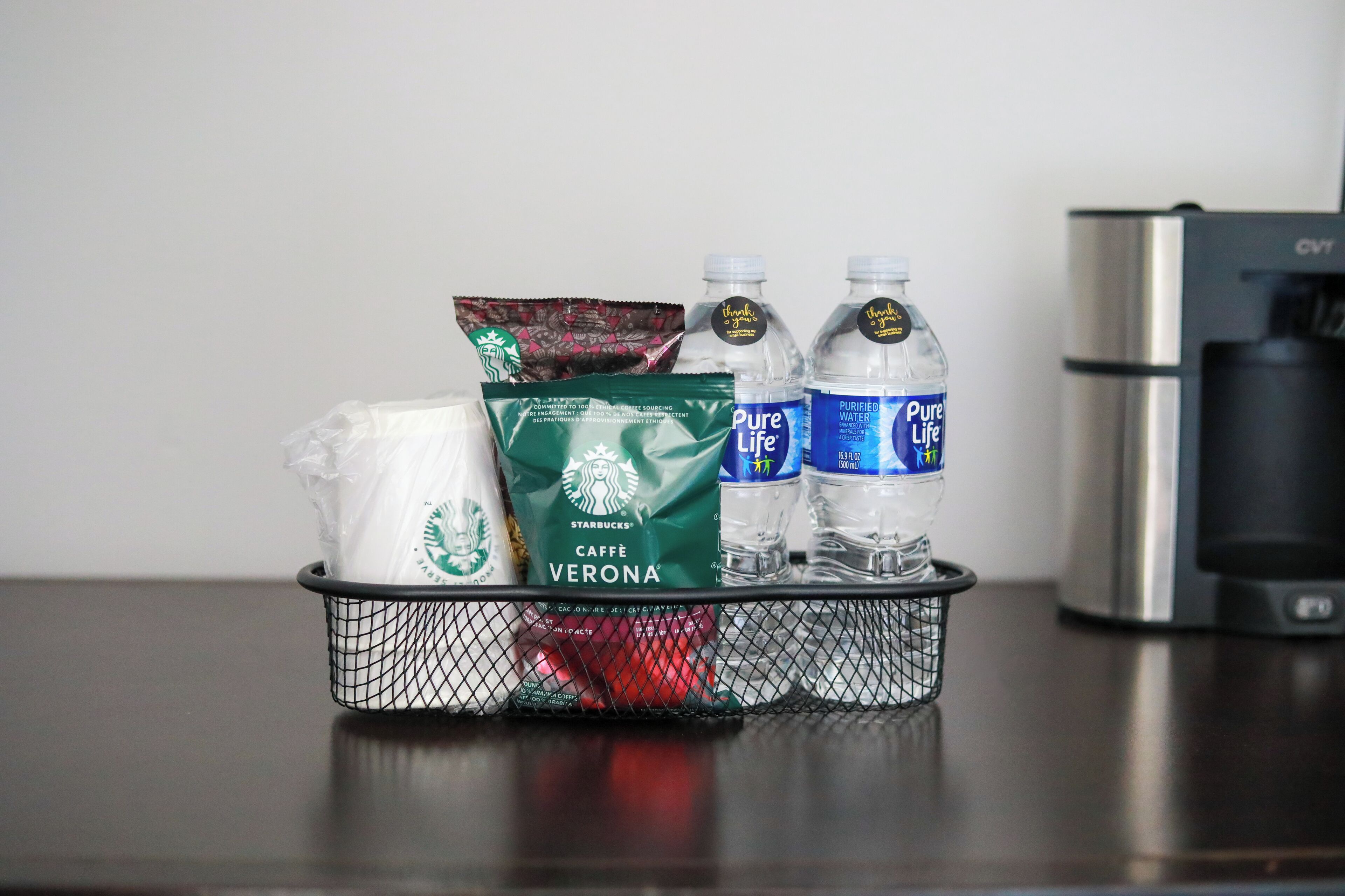 A tray with a Starbucks coffee bag, a Starbucks Caffe Verona bag, two bottles of Pure Life water, and a Starbucks napkin dispenser.