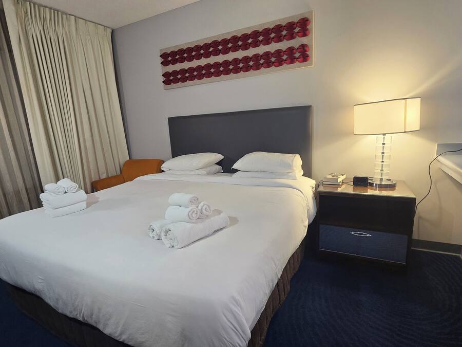 A hotel room with a neatly made bed, a bedside table with a lamp, and a wall-mounted artwork.