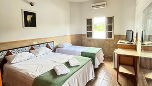 Une chambre d’hôtel avec deux lits, un bureau avec un ordinateur, un climatiseur et une fenêtre donnant sur un paysage verdoyant.