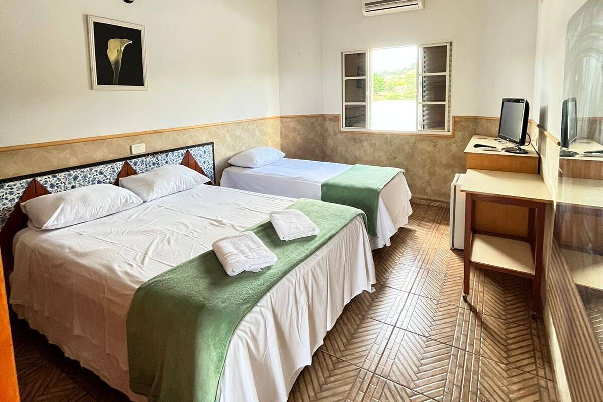 Ein Hotelzimmer mit zwei Betten, einem Schreibtisch mit Computer, einer Klimaanlage und einem Fenster mit Blick auf Grünflächen.