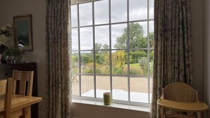 Une pièce avec une grande fenêtre, une chaise en bois, une petite table et une tasse verte posée sur le rebord de la fenêtre.