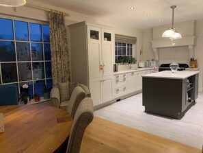 A modern kitchen with white cabinetry, a wooden dining table, and a large window with curtains. - A haven in the Orchard County. (Portadown)