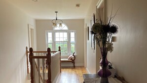 Un hall d’entrée spacieux, doté de parquets en bois, d’un banc, d’une table avec un vase et d’un escalier muni d’une rampe.