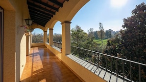 A balcony with a wooden floor, columns, and a metal railing overlooking a park and buildings. - Lake Views Quiet House, no Neighbors. Less Than 10min Walk From Beach and Shops (Platja d'Aro)