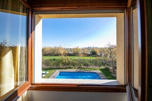 A view through a window of a backyard with a swimming pool, a grassy area, and a hedge. - Lake Views Quiet House, no Neighbors. Less Than 10min Walk From Beach and Shops (Platja d'Aro)
