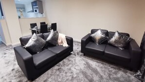 Un salon moderne avec deux canapés noirs, chacun agrémenté de coussins décoratifs argentés, et un tapis gris.