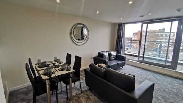 Un salon moderne avec un coin repas, une grande fenêtre donnant sur la ville et un grand miroir rond accroché au mur.