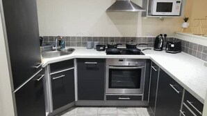 Une cuisine de taille réduite, dotée de meubles de rangement sombres, d’une hotte de cuisinière en acier inoxydable, d’un four à micro-ondes et d’un grille-pain.
