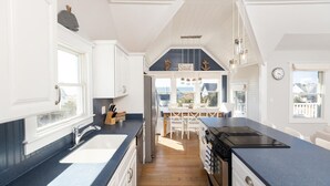 Cozinha moderna com armários brancos, bancada preta e vista para o mar através de grandes janelas.