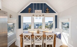 Une cuisine avec un îlot central en bois, des chaises blanches et une vue sur l’océan.