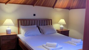 Een net opgemaakt bed met witte lakens en kussens, twee nachtkastjes met lampen, en een houten plafond.