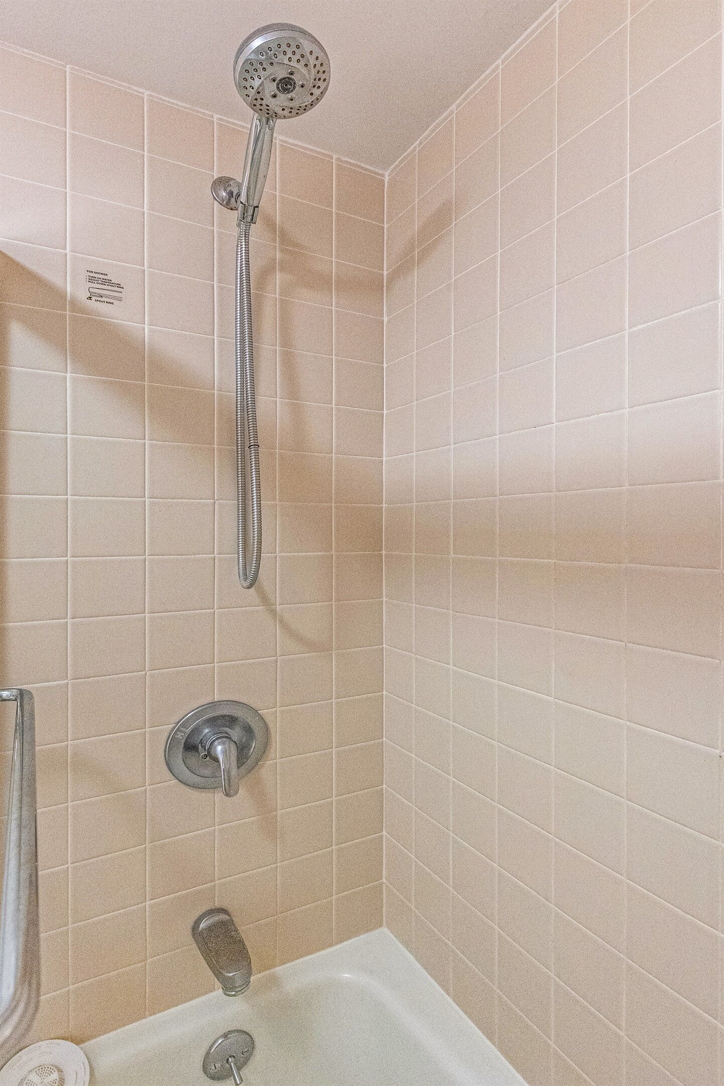 Une salle de bain avec des carreaux de couleur beige, une pomme de douche, une baignoire et des toilettes.