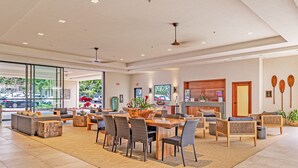 A spacious lobby with a wooden dining table, comfortable seating, and a large window offering a view of the street. - Valley Isle Resort #1107 - Vacation West Maui - Beachfront Oasis (Lahaina)