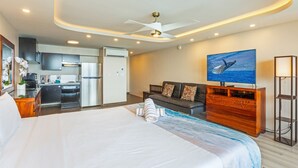 A hotel room with a bed, a TV, a sofa, a wooden cabinet, and a kitchenette in the background. - Valley Isle Resort #1107 - Vacation West Maui - Beachfront Oasis (Lahaina)