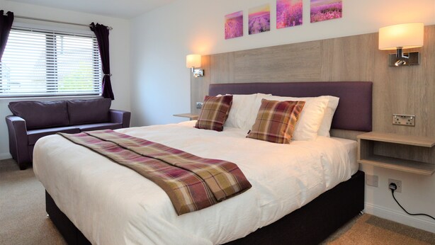 A modern bedroom with a large bed, a bedside table, a nightstand, a sofa, and a window with curtains. - Fyne Rooms - Arran Superior King - Bed & Breakfast (Tighnabruaich)