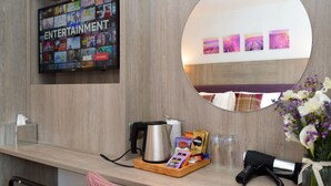 A hotel reception area with a television displaying entertainment options, a coffee machine, a tray with snacks, a hairdryer, and a mirror reflecting the room's decor. - Fyne Rooms - Arran Superior King - Bed & Breakfast (Tighnabruaich)