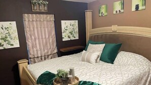 A bedroom with a bed, a bedside table, a nightstand, and a wall-mounted shelf with decorative items.