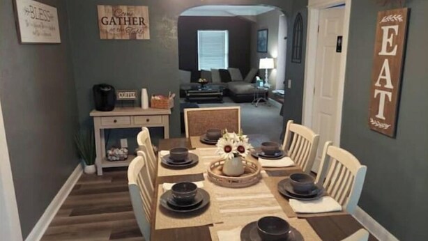 A dining area with a wooden table set for four, surrounded by white chairs.