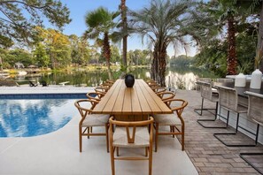 Una mesa de madera con sillas, una piscina y vistas a un lago rodeado de árboles.