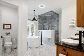 Un baño moderno con inodoro, una bañera independiente, ducha con cerramiento de vidrio y tocador doble.