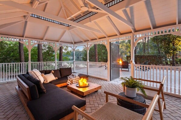A covered outdoor seating area with a sofa, chairs, and a fire pit.