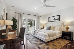 A modern hotel room with a large bed, a desk, a chair, and a ceiling fan.