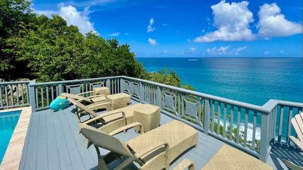 A deck with wicker chairs and a pool, overlooking a clear blue sea and lush greenery. - Villa Mangorosa (St Thomas)