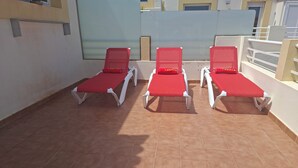 Eine Terrasse mit drei Liegestühlen, einem gefliesten Boden und einem weißen Geländer.