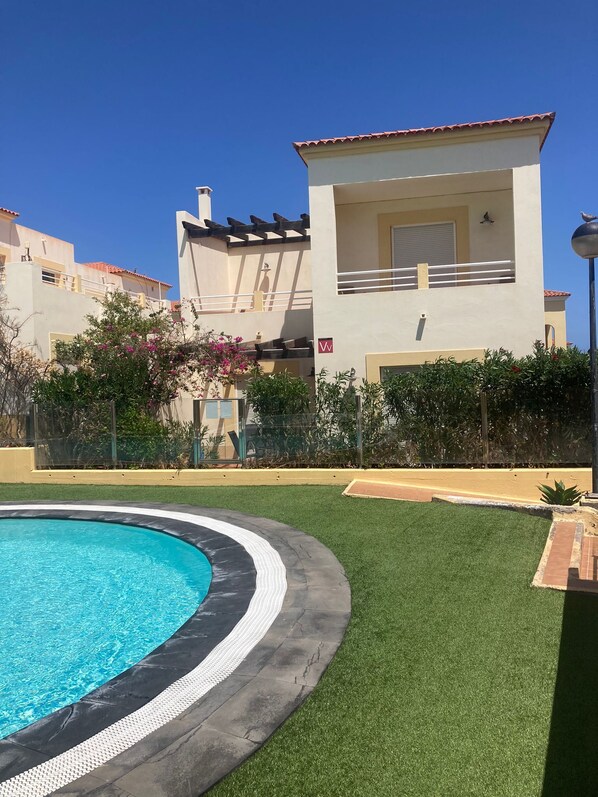A swimming pool with a surrounding grassy area and a building with a balcony. - Poolside villa with private access from terrace in secure gated community. (Castillo Caleta de Fuste)