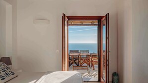 Una habitación con cama, una mesa de madera y sillas afuera, y vista al mar.