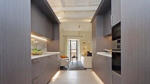Un pasillo estrecho con armarios modernos, una zona de cocina con microondas y una sala de estar con sofá y una mesita.