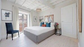 Un dormitorio moderno con una cama grande, una silla, una mesita con un florero y obras de arte en las paredes.
