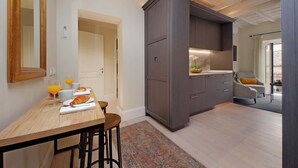 Cocina moderna con armarios oscuros, una mesa de comedor de madera con cosas para el desayuno y vistas a una sala de estar con un sillón gris.