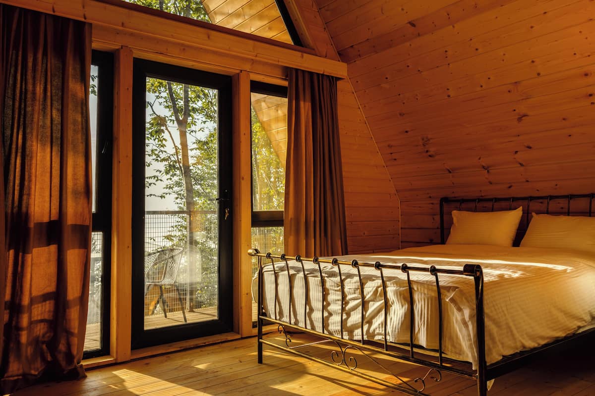 A bedroom with a bed, curtains, and a view of trees through a large window.