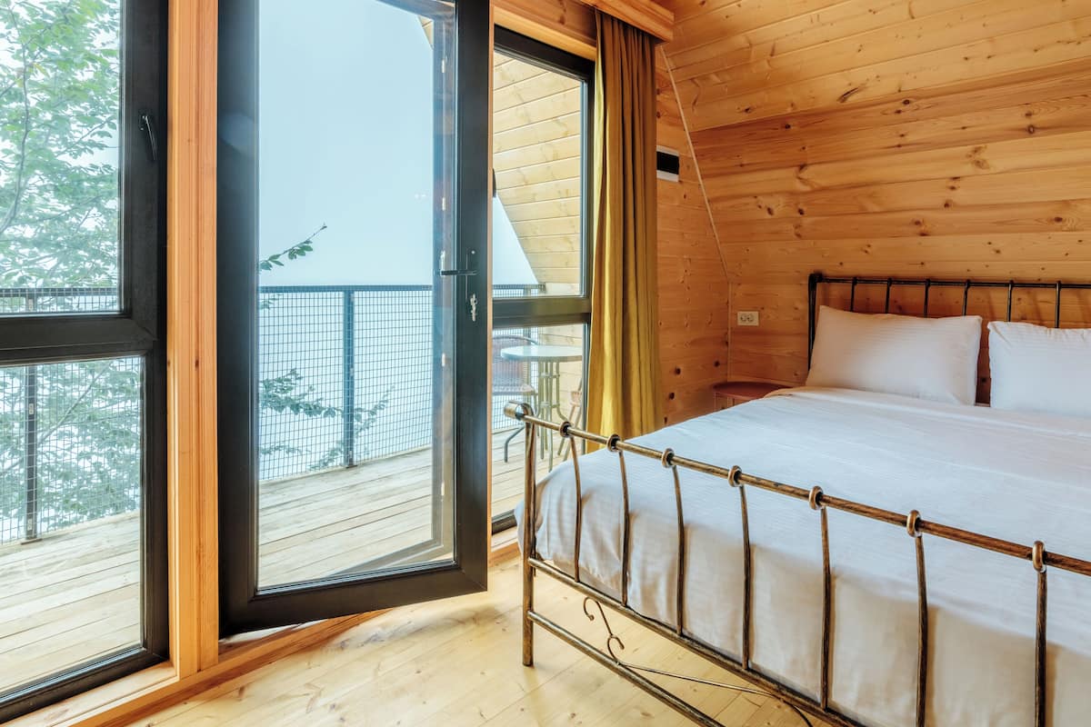 A wooden cabin room with a bed, a window, and a balcony.