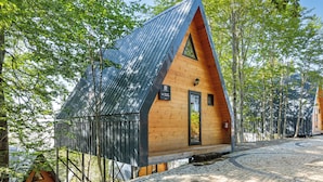 A wooden cabin with a sloped roof, surrounded by trees, and a cobblestone path leading to it. - Chalet Kvirike (Kobuleti)