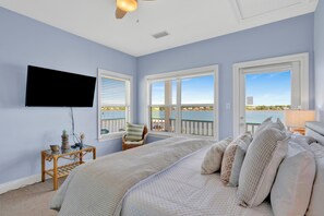 A bedroom with a bed, a television, a chair, and a view of the water.